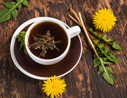 Dandelion leaf tea Zwarte thee in een witte kop met dandelionbloemen en groene bladeren eromheen.