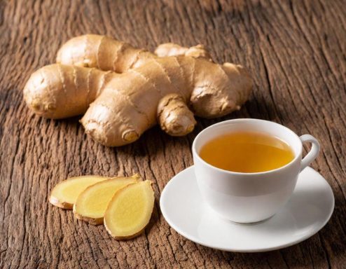 Gember thee Gemberwortels, schijfjes gember en een kopje gemberthee op een houten ondergrond.