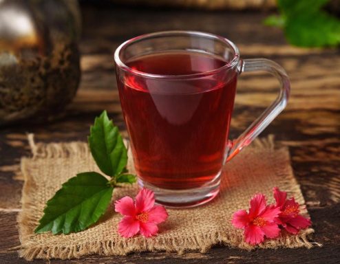 Hibiscus leaf tea Kopje met heldere, rode thee op een jute ondergrond met bloemen en bladeren.