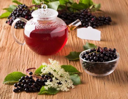 Elderberry thee Elderberry thee in een glazen pot, omringd door bessen en bladeren op een houten oppervlak.